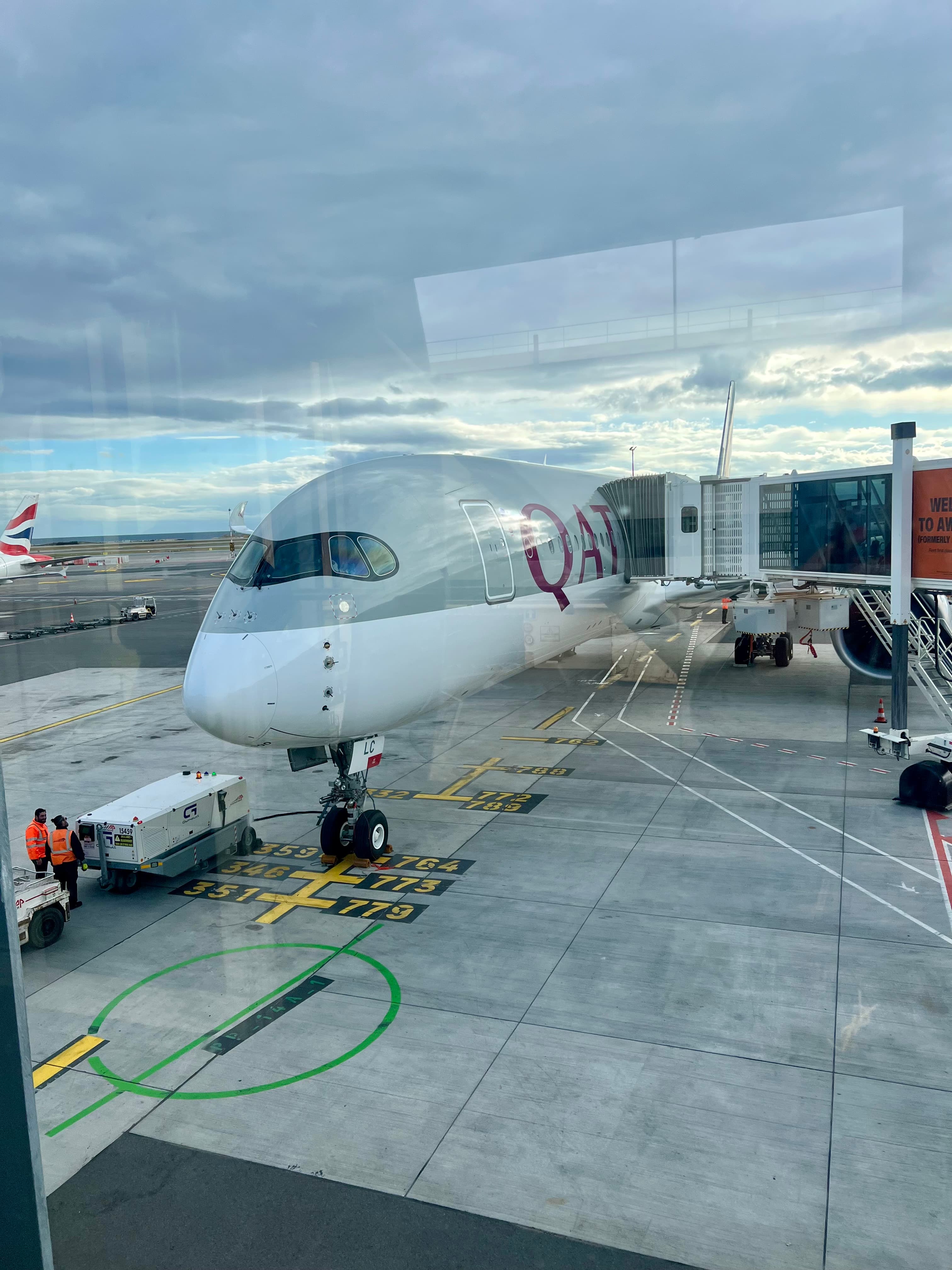 Nose of a Qatar Airways Airbus A350 parked at a boarding bridge.