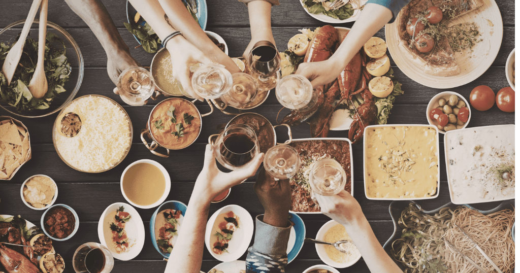 Plusieurs personnes trinquent autour d'une table garnie de plats partagés, vue du dessus
