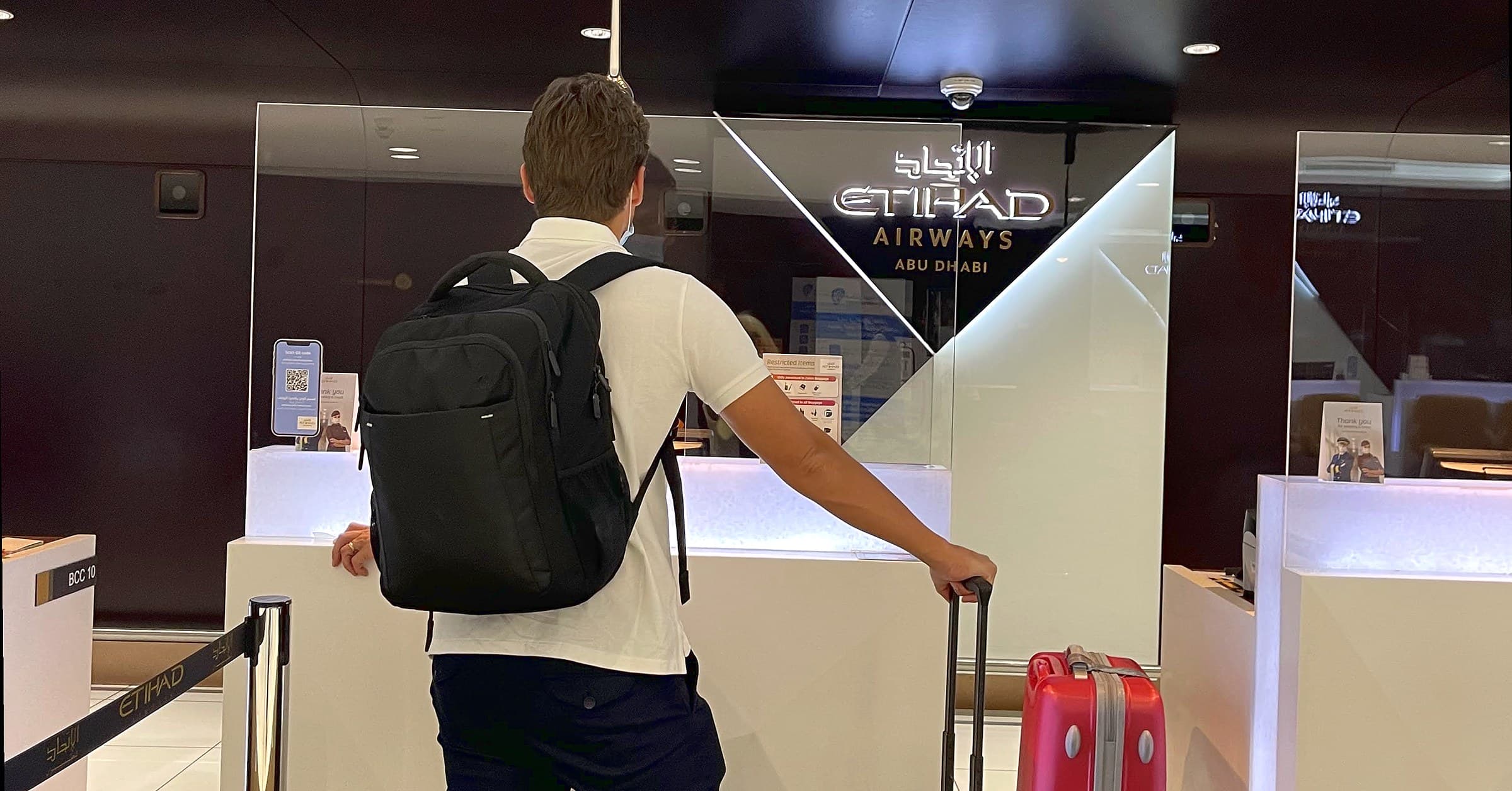 Traveller with a black carry-on backpack at the Etihad Airways check-in counter at Abu Dhabi airport