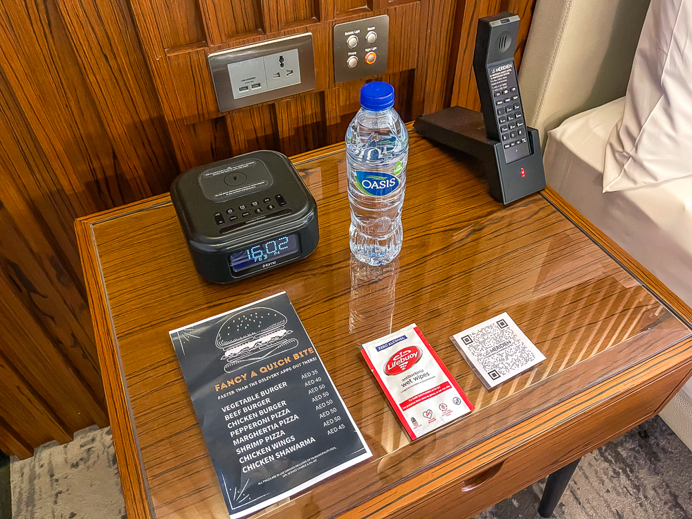 Table de chevet avec radio-réveil et eau offerte dans une chambre du le meridien dubai hotel conference