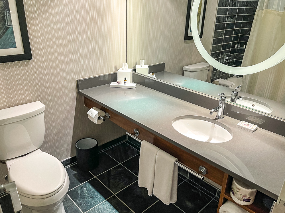 Salle de bain contemporaine au hyatt regency vancouver avec grand lavabo, miroir rond et carrelage noir