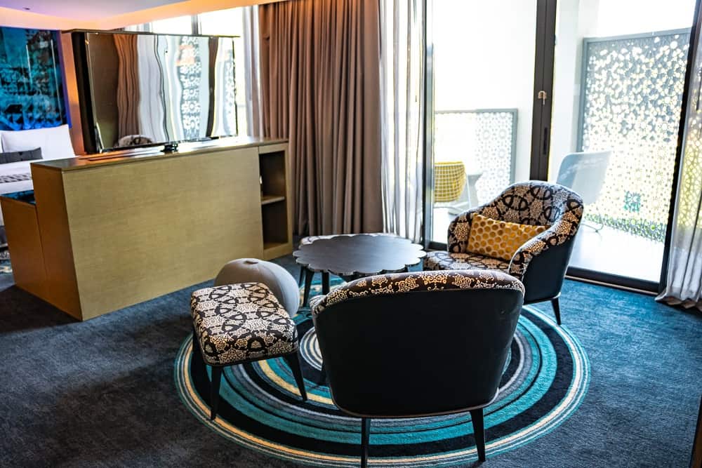 Salon du w muscat avec fauteuils à motifs géométriques dorés, tapis circulaire et vue sur l'extérieur, décoration contemporaine