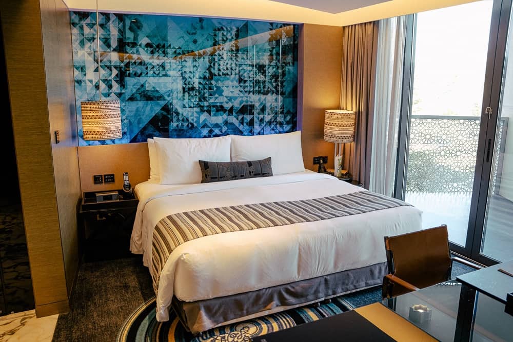 Chambre king-size du w muscat avec tête de lit géométrique bleue, baies vitrées panoramiques et décoration contemporaine luxueuse