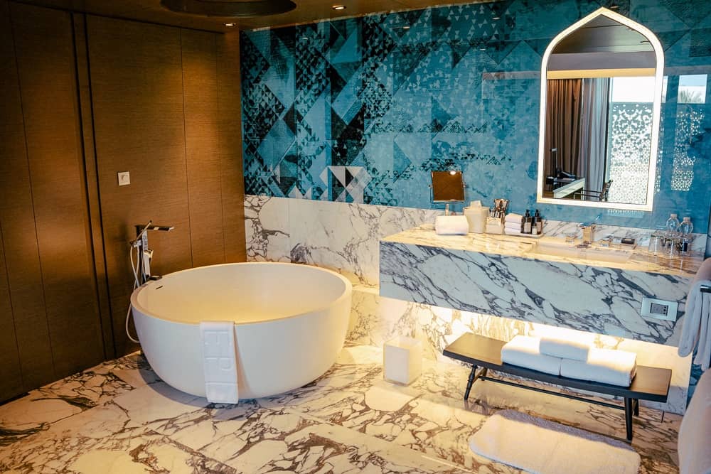 Salle de bain panoramique du w muscat avec baignoire îlot, carrelage bleu géométrique et miroir arqué de style omanais