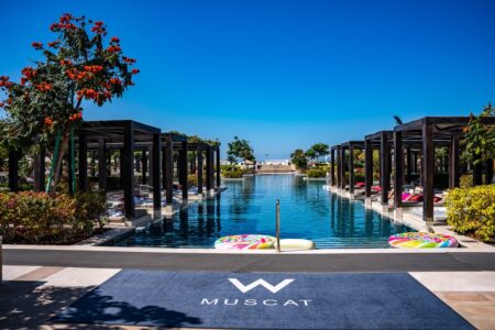 Piscine à débordement du w muscat avec cabanes privatives noires, logo W au sol et bouées colorées sous ciel azur