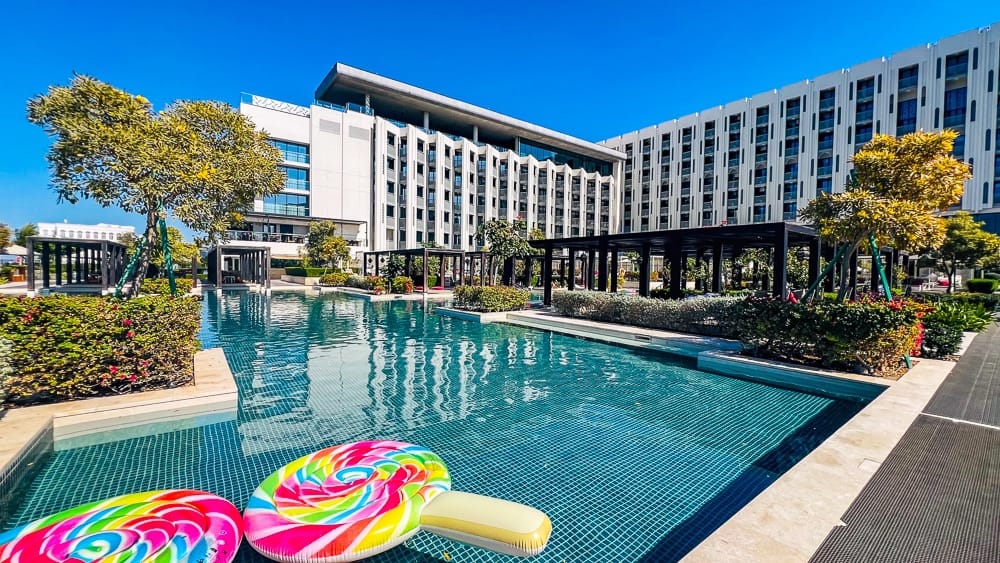 Piscine principale du w muscat avec bouées colorées en forme de sucettes, cabanes noires et façade moderne de l'hôtel