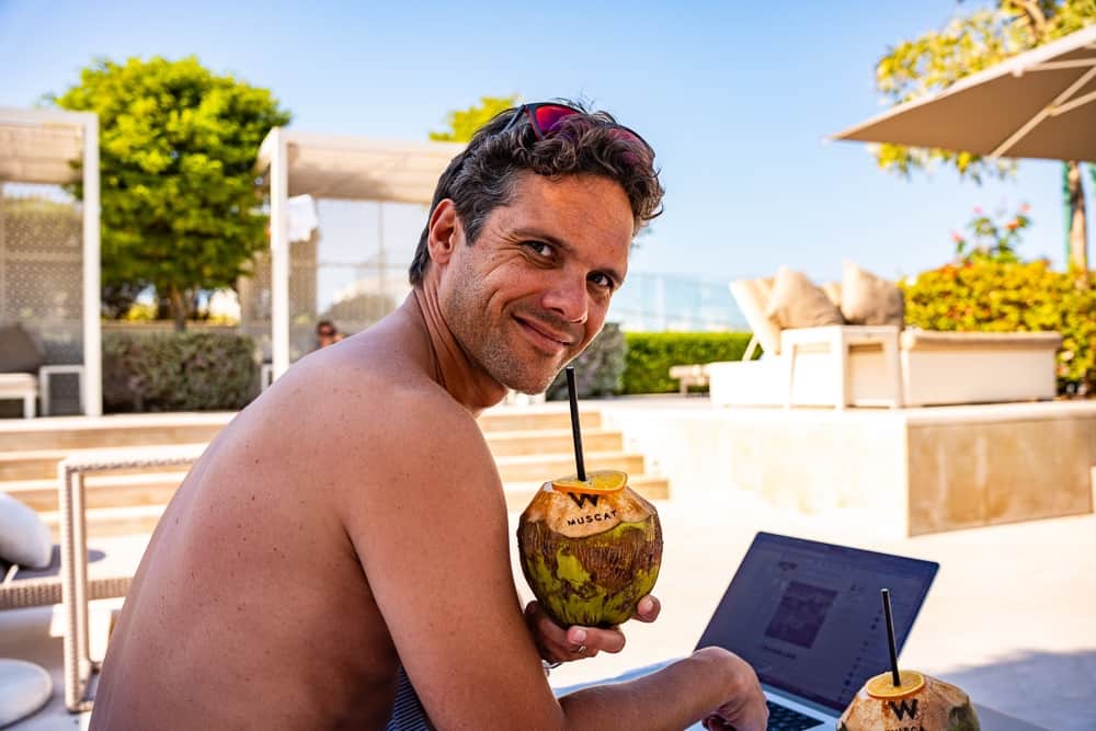 Client du w muscat savourant une noix de coco fraîche au bord de la piscine avec ordinateur portable, ambiance détendue
