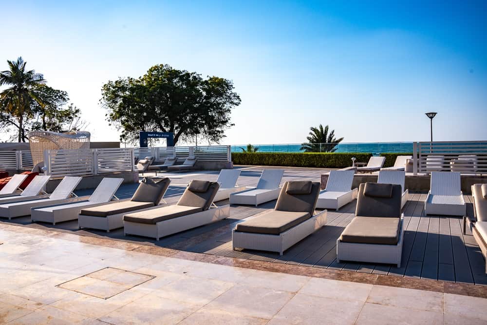 Terrasse solarium du w muscat avec transats blancs alignés, parasols beiges et vue imprenable sur la mer d'Arabie
