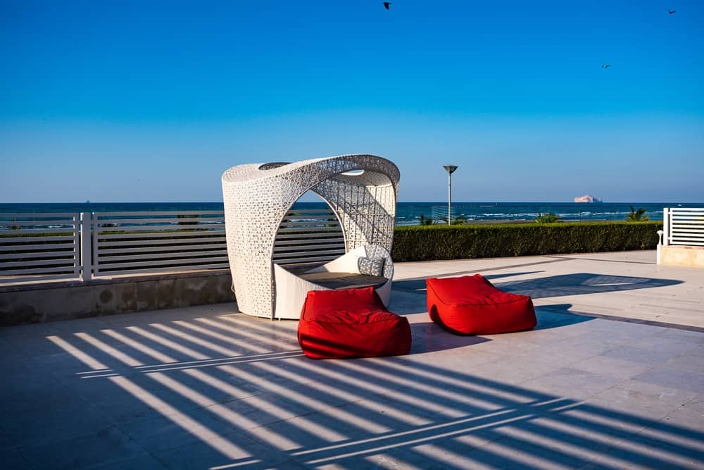 Cabane design moderne du w muscat avec structure blanche ajourée, coussins rouges et vue panoramique sur la mer d'Arabie