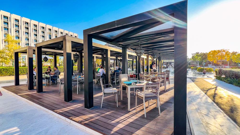 Terrasse extérieure du restaurant w muscat avec pergola noire moderne, tables et chaises design sous un ciel bleu azur