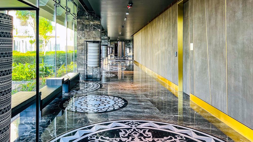 Couloir design du w muscat avec sol en marbre noir et blanc, plafond sophistique et vue sur jardin tropical