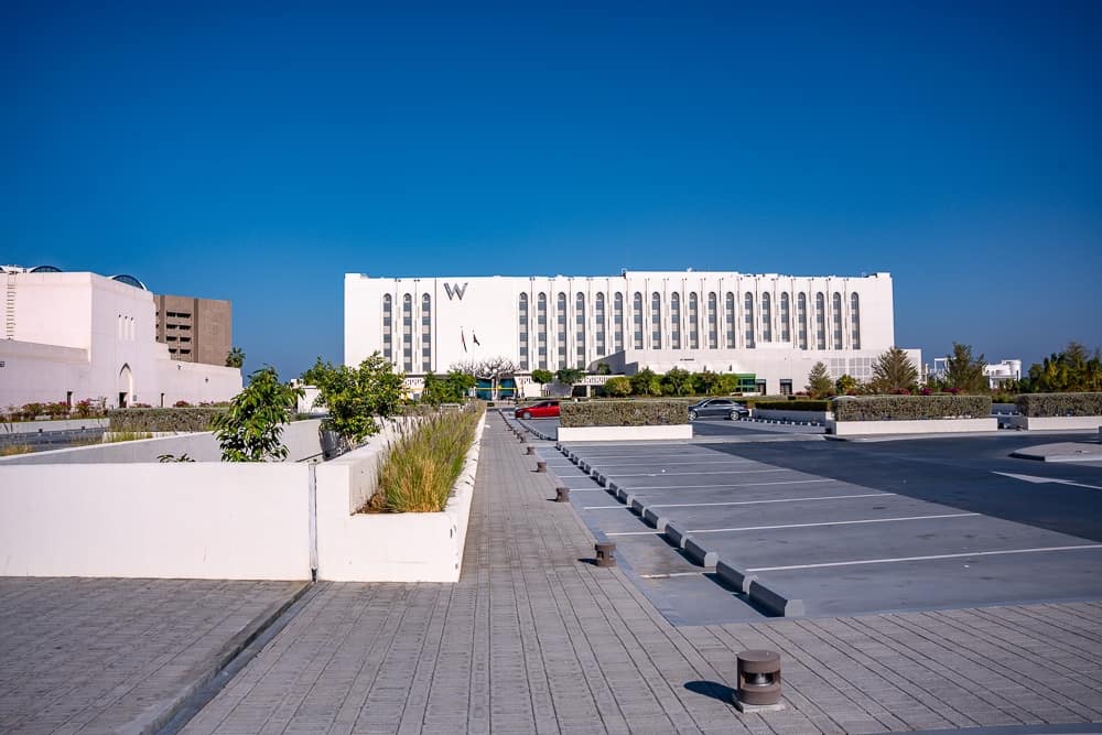 Vue exterieure sur l'Opera Royal d'Oman avec parking et hotel w muscat en arriere-plan sous un ciel bleu eclatant