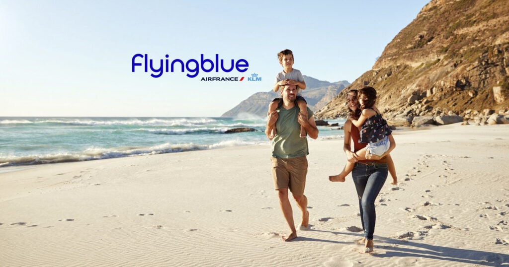 Mid adult white couple walking along on a beach on a family holiday carrying their kids, full length