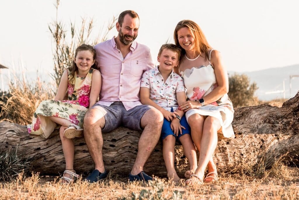 Une famille avec deux enfants en train de sourire, assis sur un tronc d'arbre