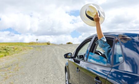 Une voiture sur une route avec une personne à l'arrière qui brandit un chapeau