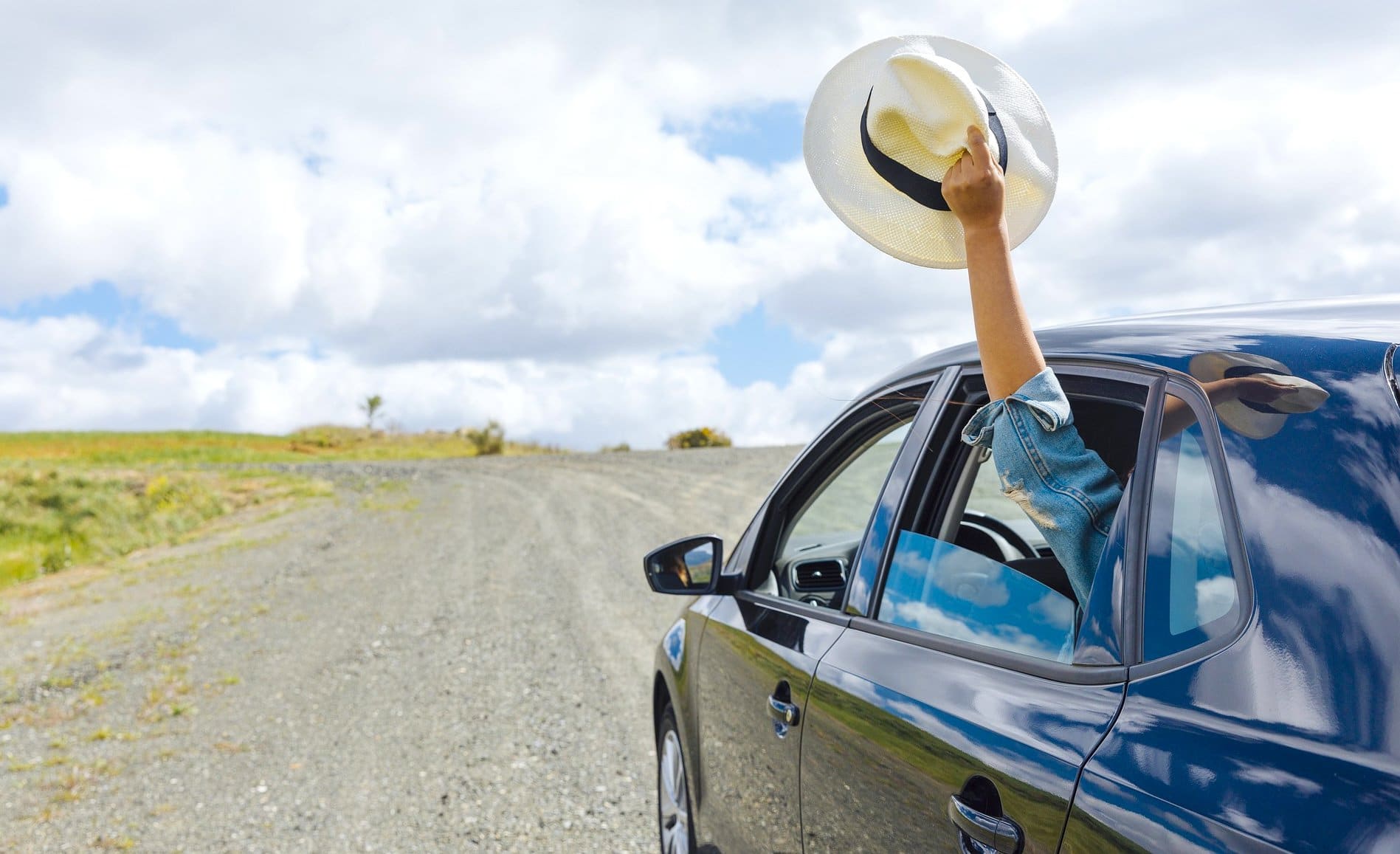 Une voiture sur une route avec une personne à l'arrière qui brandi un chapeau