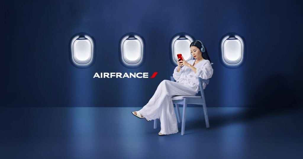 Un femme est assise sur une chaise, avec un fond de hublot et le logo Air France