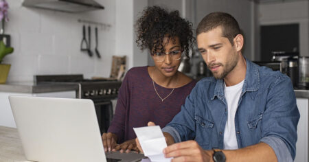 Jeune couple qui examine leur finance à la maison devant l'ordinateur portable dans la cuisine