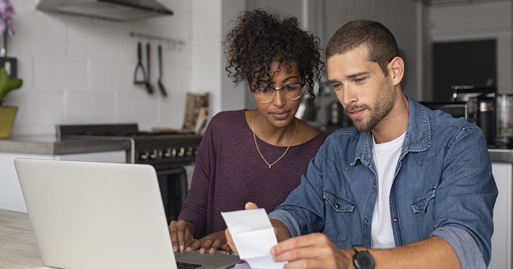 Jeune couple qui examine leur finance à la maison devant l'ordinateur portable dans la cuisine