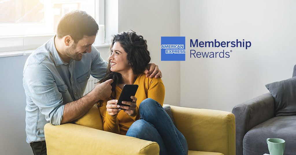 A smiling couple chatting on a sofa with a telephone, American Express Membership Rewards logo visible.