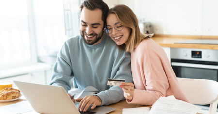 Un couple souriant effectue des achats en ligne avec un ordinateur portable et une carte de crédit dans leur cuisine