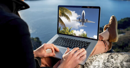 Un homme regardant un avion décoller sur son ordinateur portable, assis en plein air.