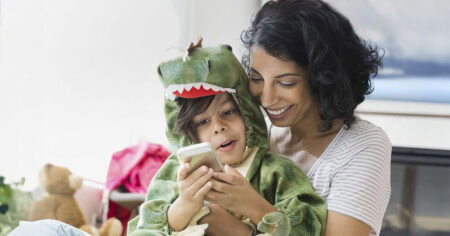 Une femme sourit en regardant un téléphone avec un enfant déguisé en dinosaure