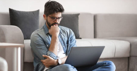 Un homme assis sur le sol semble réfléchir devant son ordinateur portable