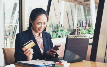 Woman with card and phone at desk with computer