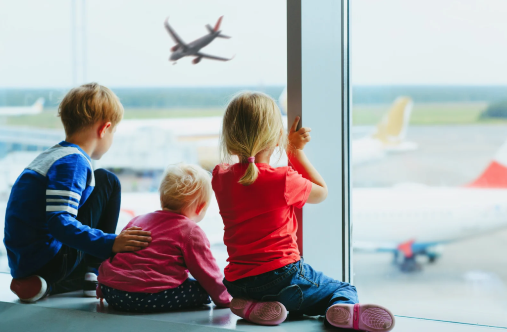 3 children looking out window at tarmac