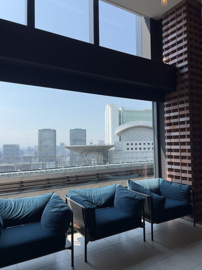 Salon moderne du Autograph Osaka avec fauteuils bleus face aux baies vitrées donnant sur le skyline d'Osaka