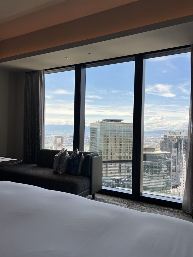 Chambre spacieuse du Autograph Osaka avec lit king-size, salon et vue panoramique sur les gratte-ciels d'Osaka