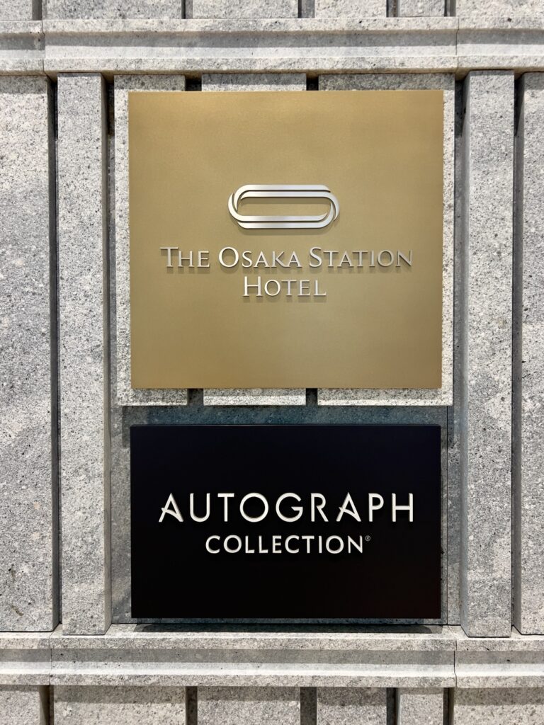 Plaque de signalisation dorée de l'Autograph Osaka et The Osaka Station Hotel sur façade en granit