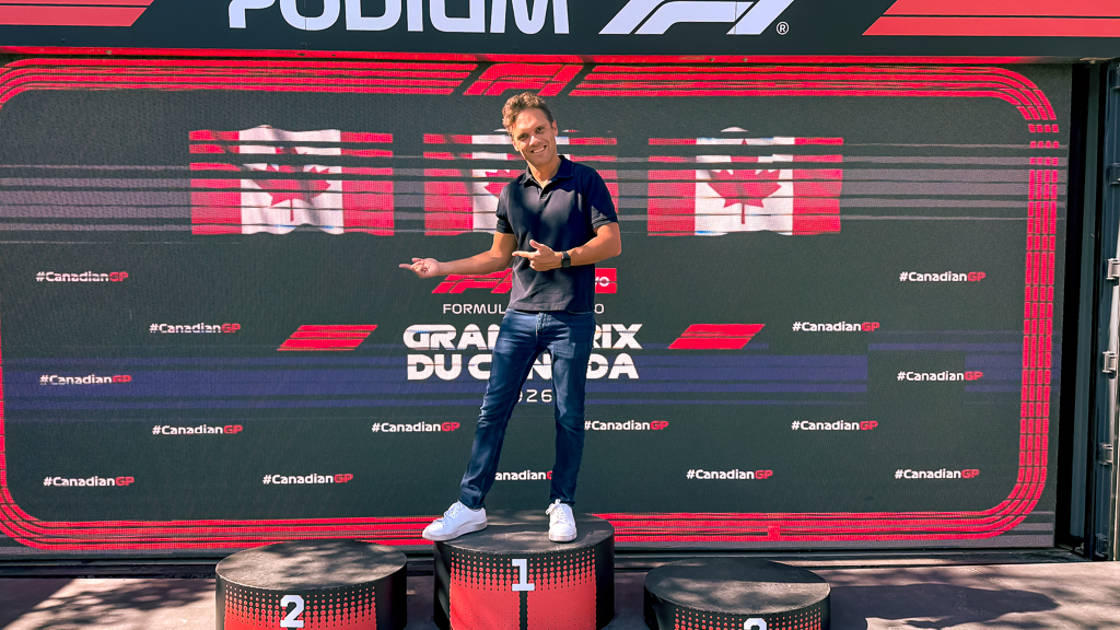 Visiteur posant sur le podium officiel F1 devant l'ecran Grand Prix du Canada avec drapeaux