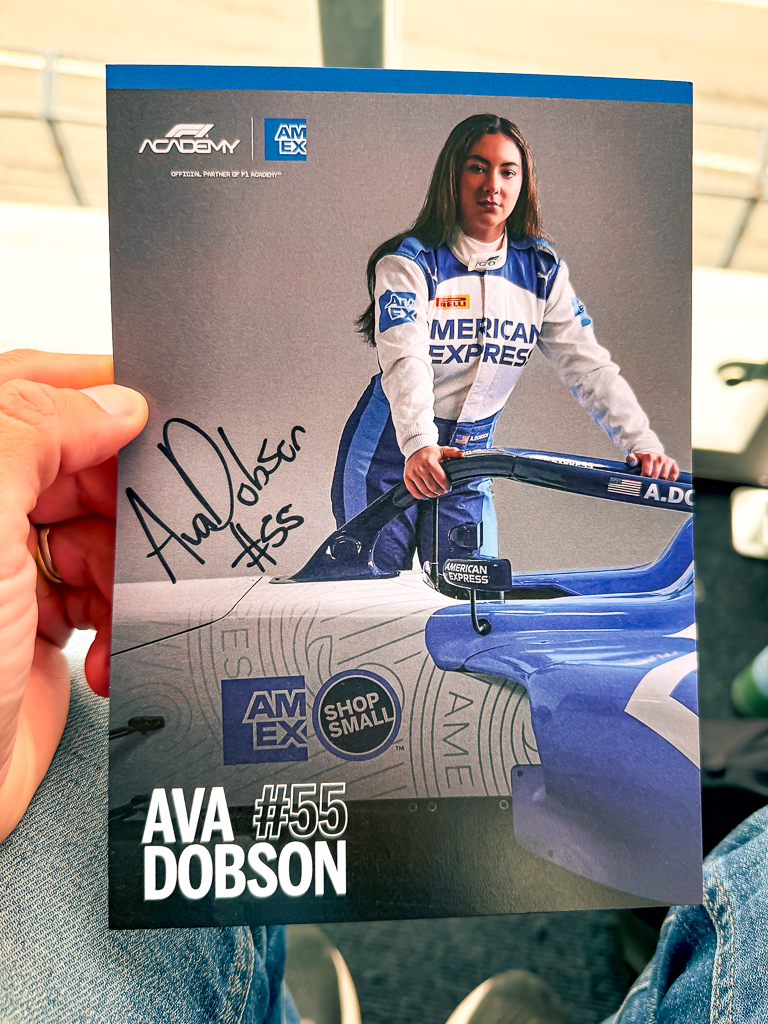Carte autographiée d'Ava Dobson pilote F1 numéro 55 en combinaison American Express bleu et blanc tenue dans une main