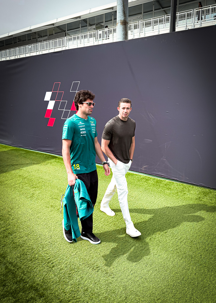 Deux pilotes F1 marchent sur l'herbe artificielle du paddock du Grand Prix de Montréal avec mur graphique en arrière-plan