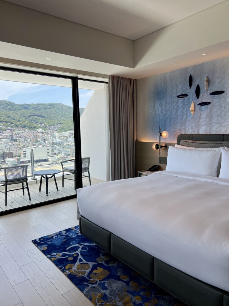 Chambre du marriott nagasaki avec lit king-size, terrasse privée et vue dégagée sur les montagnes de Nagasaki