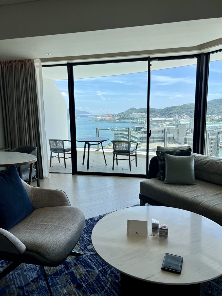 Vue d'ensemble du salon d'une suite du marriott nagasaki avec canapé d'angle et vue complète sur la baie de Nagasaki