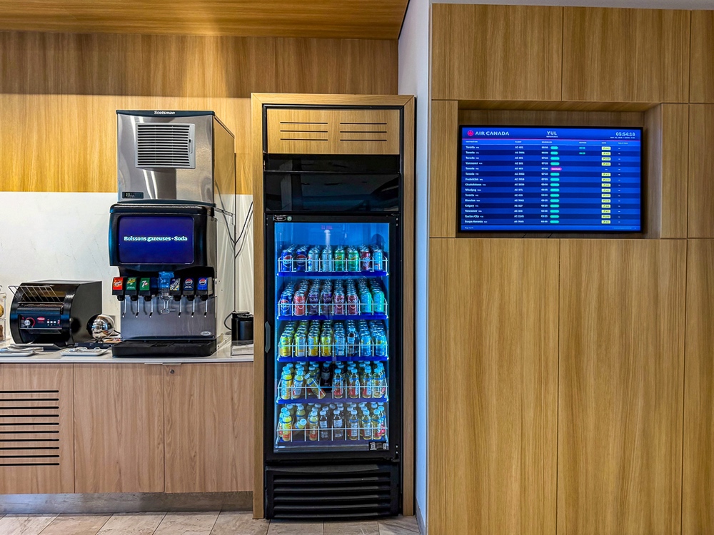 Station self-service boissons du salon air canada avec réfrigérateur transparent et écrans d'information vols
