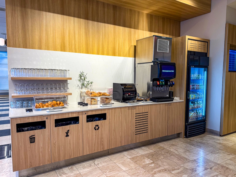 Espace restauration moderne du salon air canada avec buffet, distributeurs de boissons et refrigerateurs en bois clair