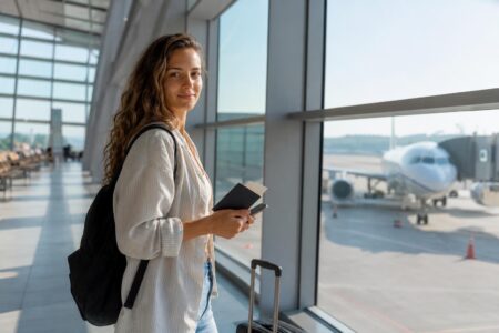 Woman traveler holding a passport and phone at an airport gate during the 2026 FIFA World Cup season