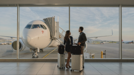 Couple de voyageurs avec valises dans un terminal d'aéroport regardant un avion sur le tarmac au départ du Canada vers l'Europe