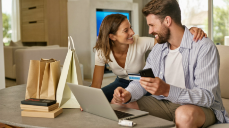 Couple souriant qui magasine en ligne à la maison avec ordinateur portable, téléphone et carte de crédit
