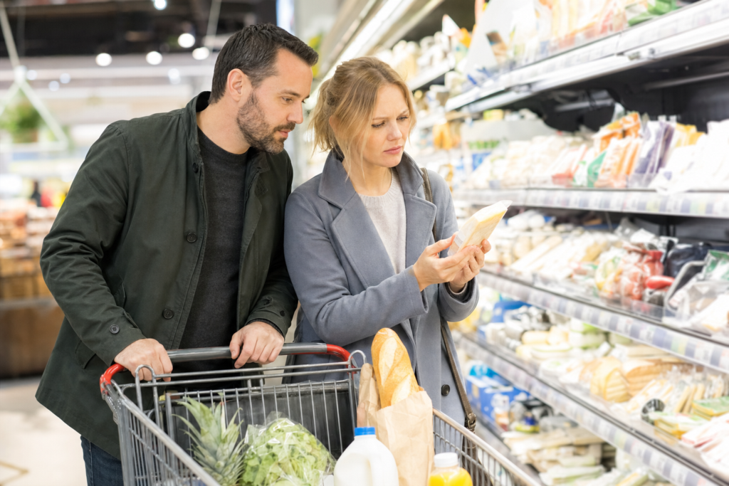 A couple grocery shopping, examining the price of a product, in the context of rising food prices in Canada