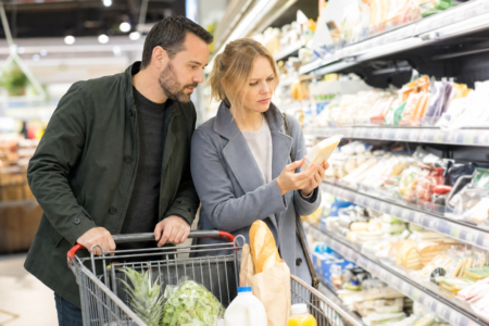 Un couple fait ses courses à l'épicerie et examine le prix d'un produit, dans un contexte de hausse des prix alimentaires au Canada