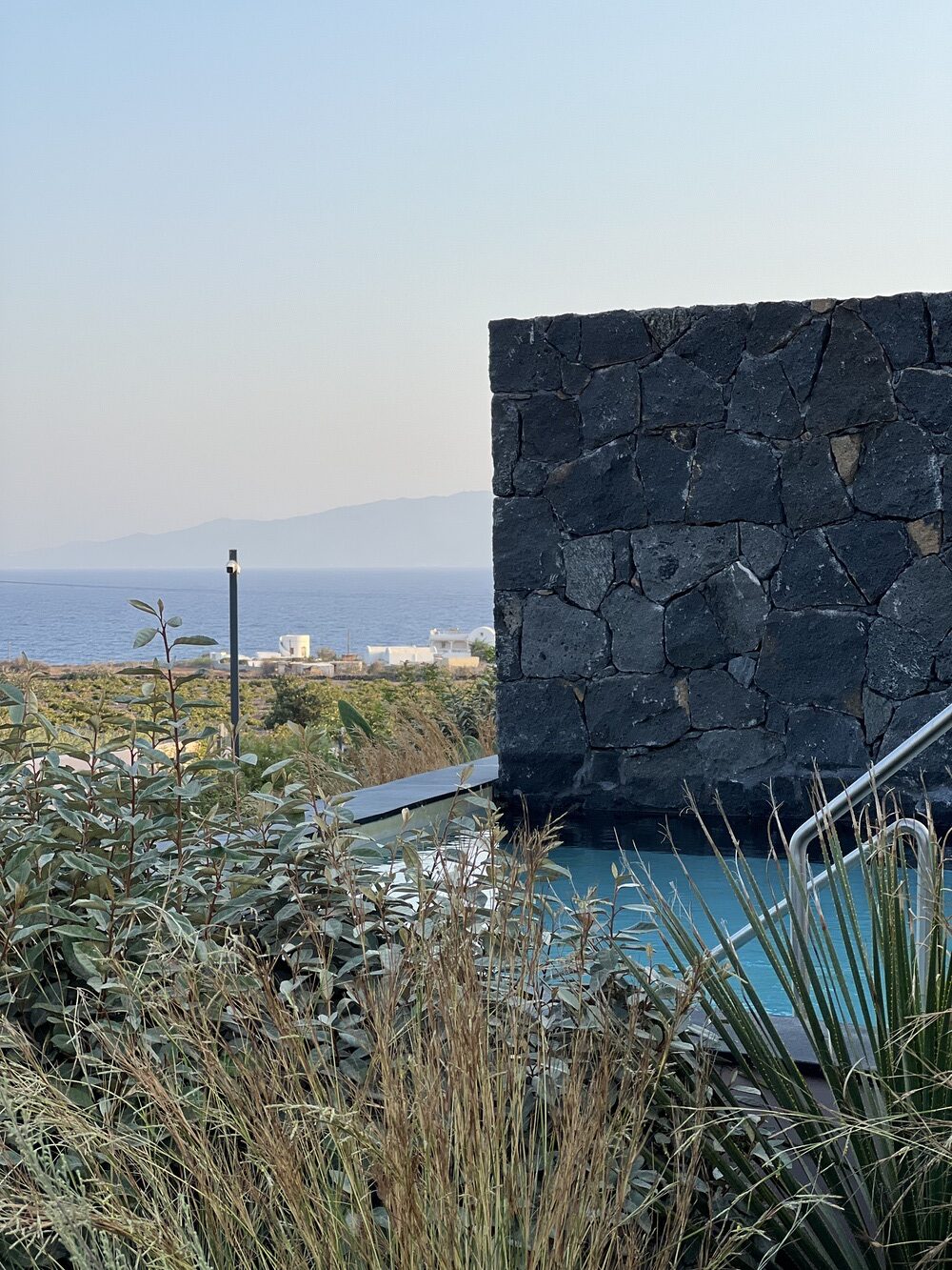 Private pool bordered by volcanic stone wall, sea view