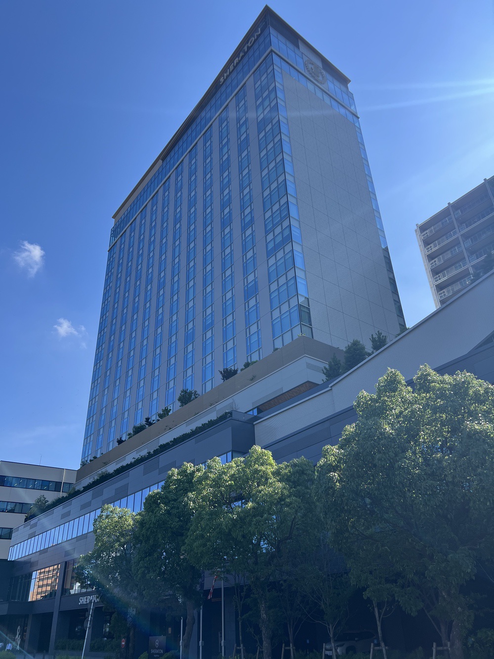 Façade moderne en verre du Sheraton Kagoshima sous un ciel bleu
