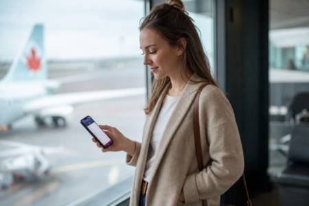Voyageuse consultant l'application de transfert de points Rove Miles près d'une porte d'embarquement Air Canada