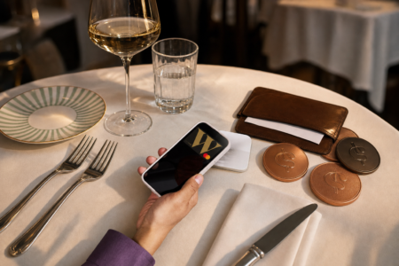 Main tenant un téléphone au terminal de paiement sur une table de restaurant, entourée de pièces cuivrées