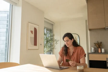 Femme payant une facture en ligne avec une carte de credit dans un condo lumineux
